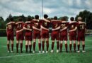 group of men in red and black jersey shirt and shorts standing on green grass field